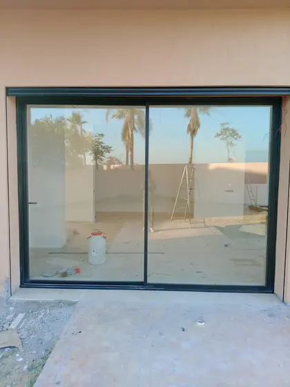 Baie vitrée coulissante aluminium ouvrant sur une terrasse bordée de palmiers