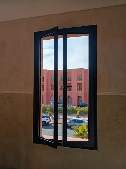 Fenêtre aluminium noire à deux vantaux posée dans une façade en pisé