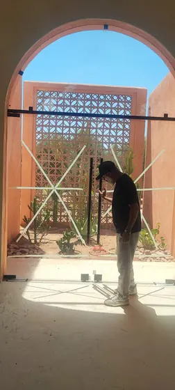 Technicien ajustant une porte en verre sous une arche de riad